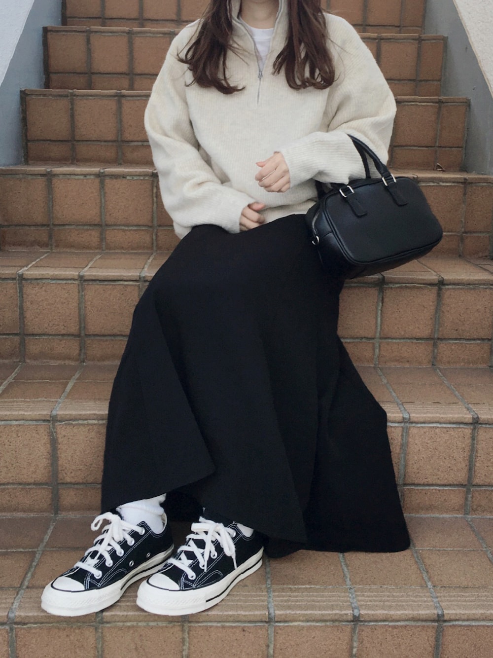 ホワイト系のトップス、ブラック系のスカート、ブラック系のスニーカーを着用したレディースの秋コーディネートの1枚目の写真