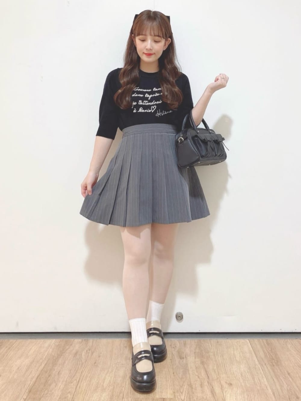 グレー系のスカート、ブラック系のハンドバッグ、ブラック系のローファーを着用したレディースの秋コーディネートの1枚目の写真