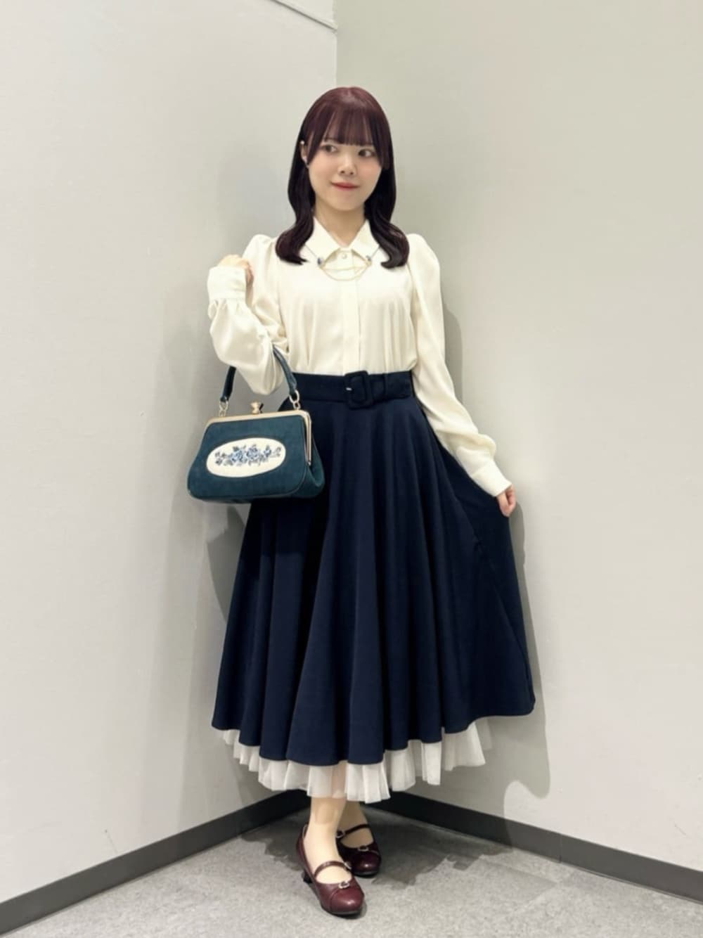 ブルー系のスカート、ブルー系のハンドバッグ、レッド系のパンプスを着用したレディースの秋コーディネートの1枚目の写真