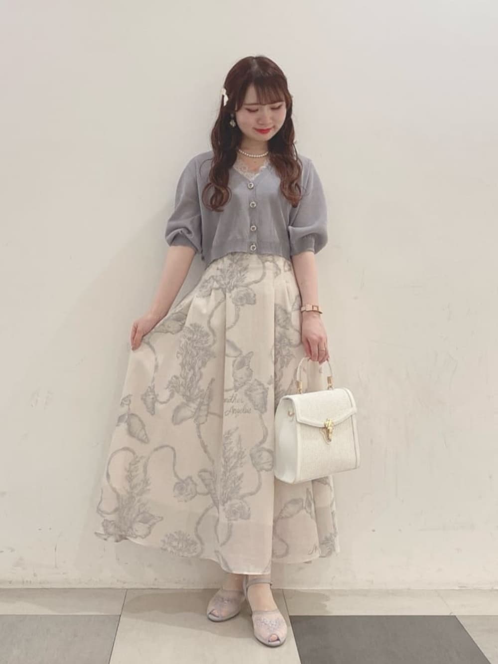 ホワイト系のハンドバッグ、ホワイト系のスカート、グレー系のカーディガン/ボレロを着用したレディースの夏コーディネートの1枚目の写真