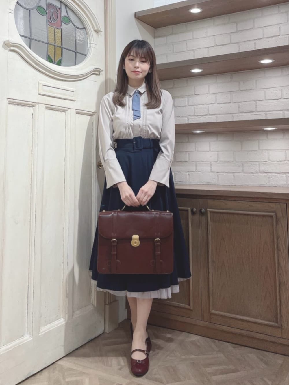 レッド系のパンプス、ベージュ系のシャツ/ブラウス、ブラウン系のハンドバッグを着用したレディースの冬コーディネートの1枚目の写真