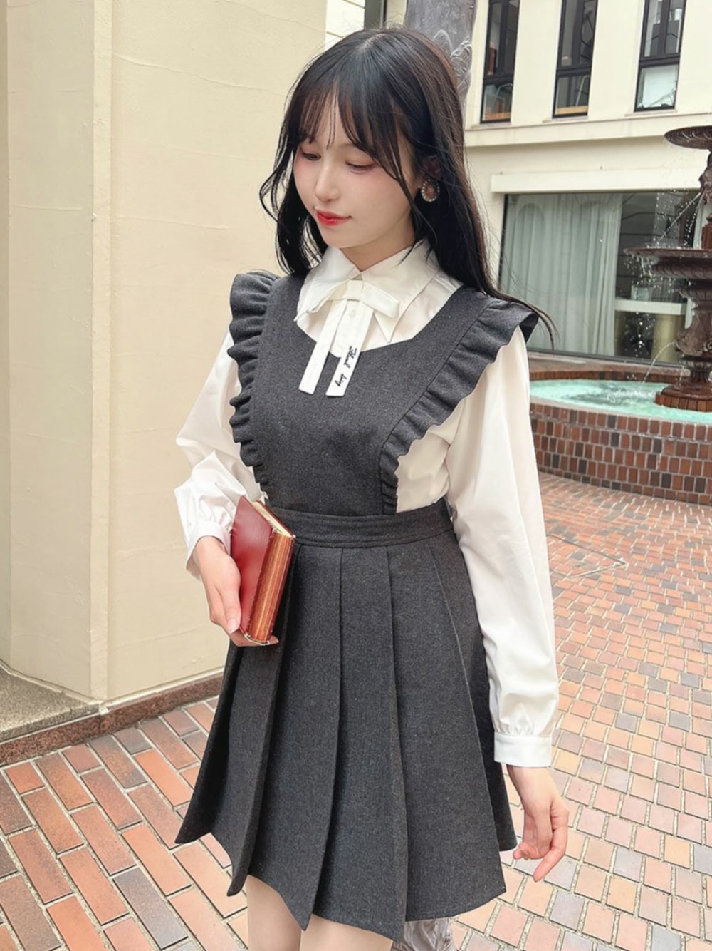 ブラック系のパンプス、グレー系のジャンパースカート、ホワイト系のシャツ/ブラウスを着用したレディースの秋コーディネートの1枚目の写真