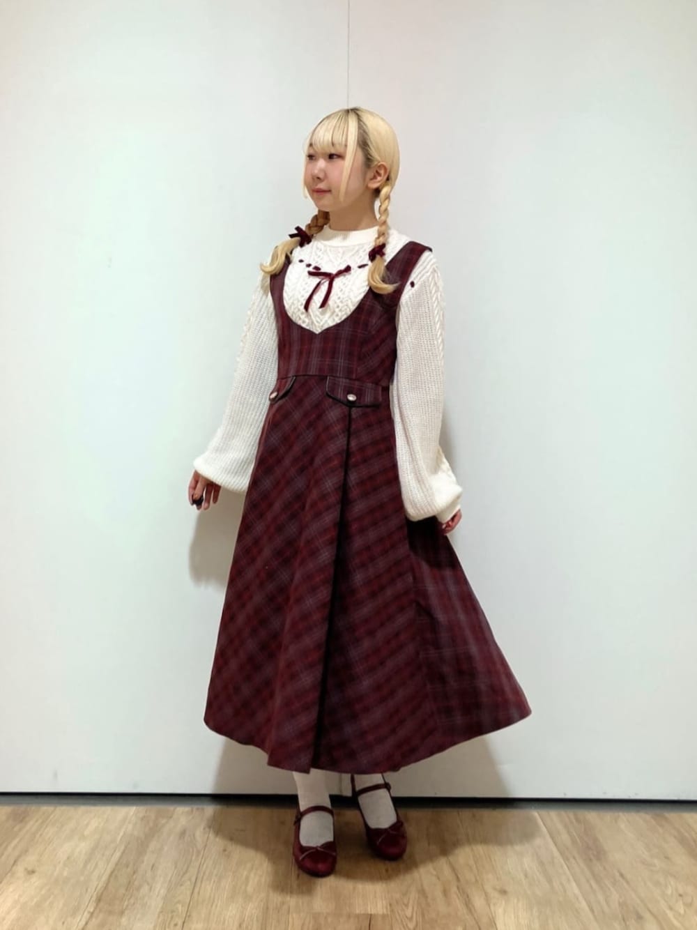 レッド系のバレエシューズ、ホワイト系のニット/セーター、レッド系のジャンパースカートを着用したレディースの冬コーディネートの1枚目の写真