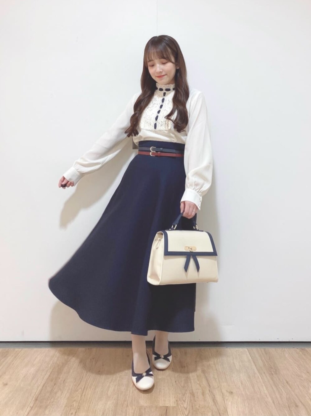 ブルー系のスカート、ホワイト系のハンドバッグ、ホワイト系のパンプスを着用したレディースの春コーディネートの1枚目の写真
