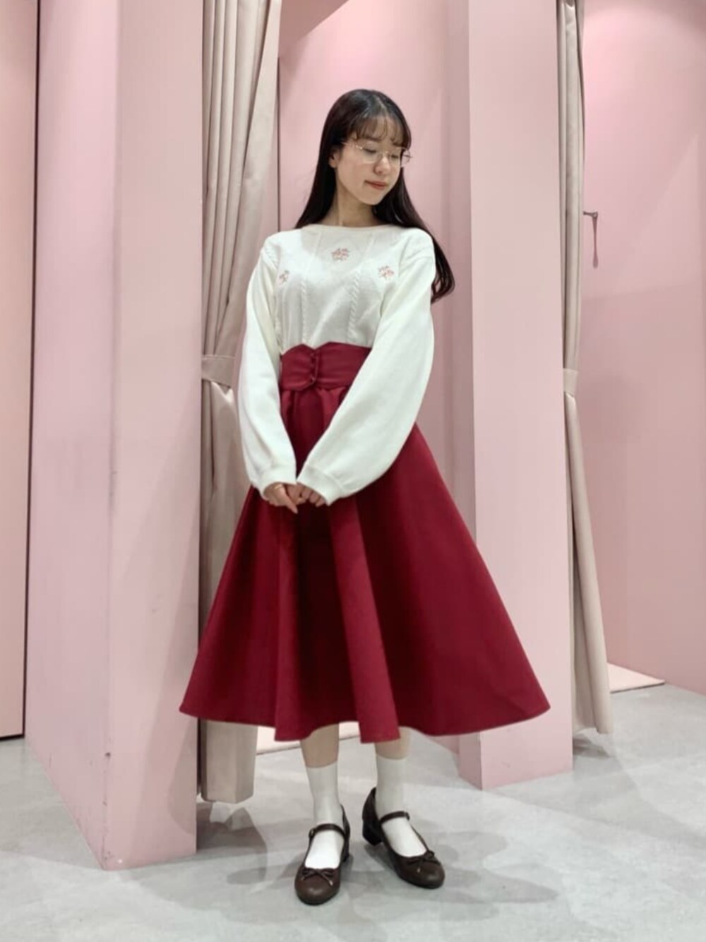 レッド系のスカート、ブラウン系のパンプス、ホワイト系のニット/セーターを着用したレディースの冬コーディネートの1枚目の写真