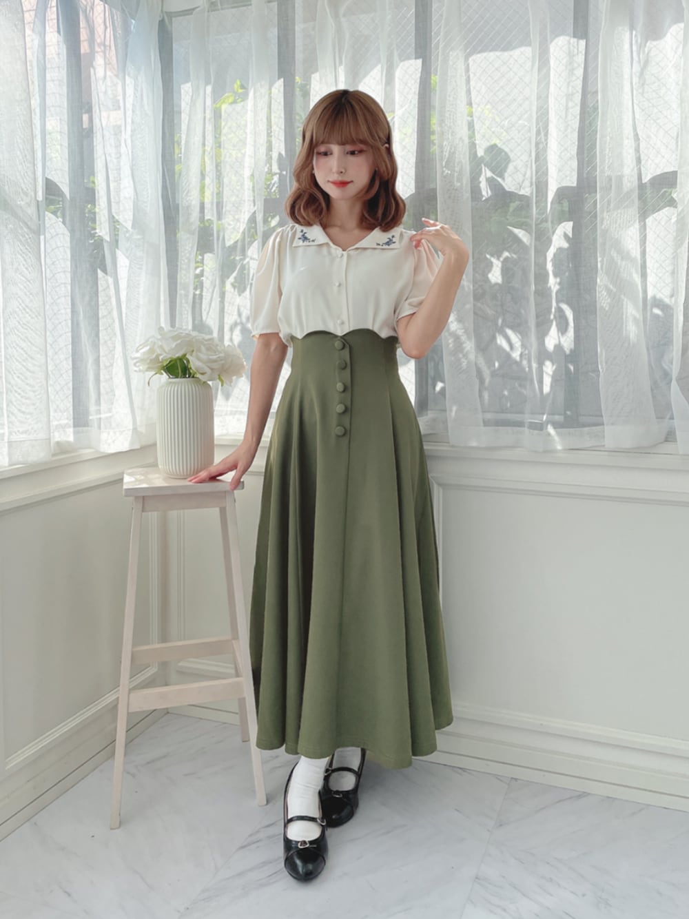 ホワイト系のシャツ/ブラウス、グリーン系のスカート、ブラック系のパンプスを着用したレディースの秋コーディネートの1枚目の写真