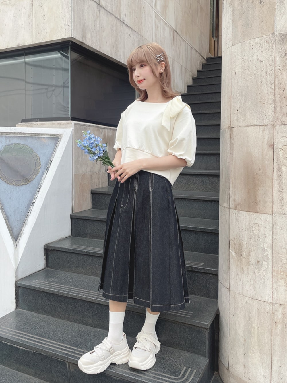 ホワイト系のスニーカー、ブラック系のデニムスカート、ホワイト系のTシャツ/カットソーを着用したレディースの春コーディネートの1枚目の写真