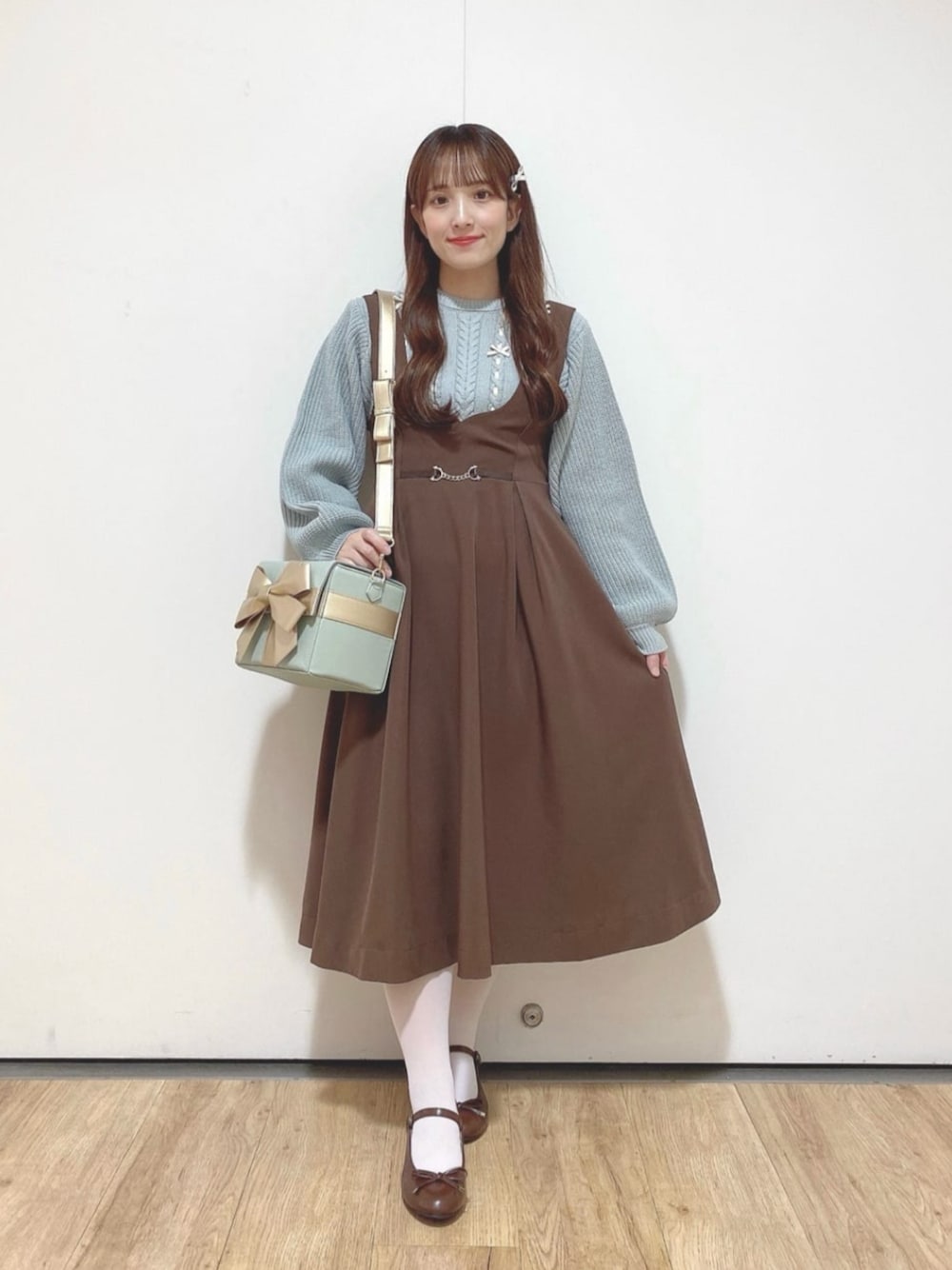 ブラウン系のジャンパースカート、ブラウン系のバレエシューズ、グリーン系のショルダーバッグを着用したレディースの冬コーディネートの1枚目の写真