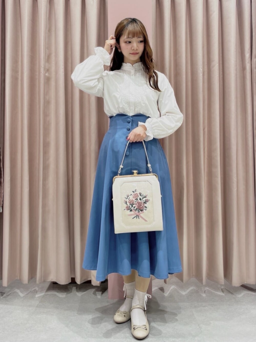 ベージュ系のパンプス、ホワイト系のハンドバッグ、ブルー系のスカートを着用したレディースの冬コーディネートの1枚目の写真