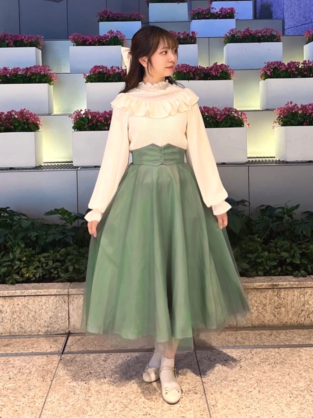 ベージュ系のパンプス、ホワイト系のニット/セーター、グリーン系のスカートを着用したレディースの冬コーディネートの1枚目の写真