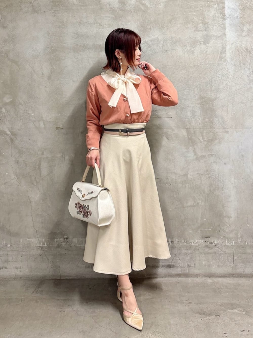 ピンク系のシャツ/ブラウス、ホワイト系のハンドバッグ、ベージュ系のスカートを着用したレディースの冬コーディネートの1枚目の写真