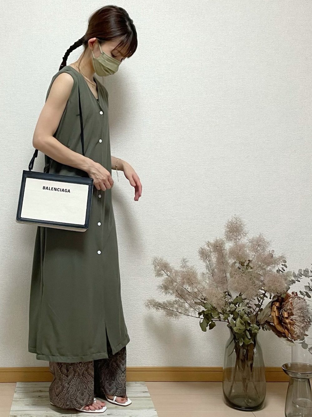 ブラック系のスラックス、ホワイト系のサンダル、ホワイト系のクラッチバッグを着用したレディースの秋コーディネートの1枚目の写真