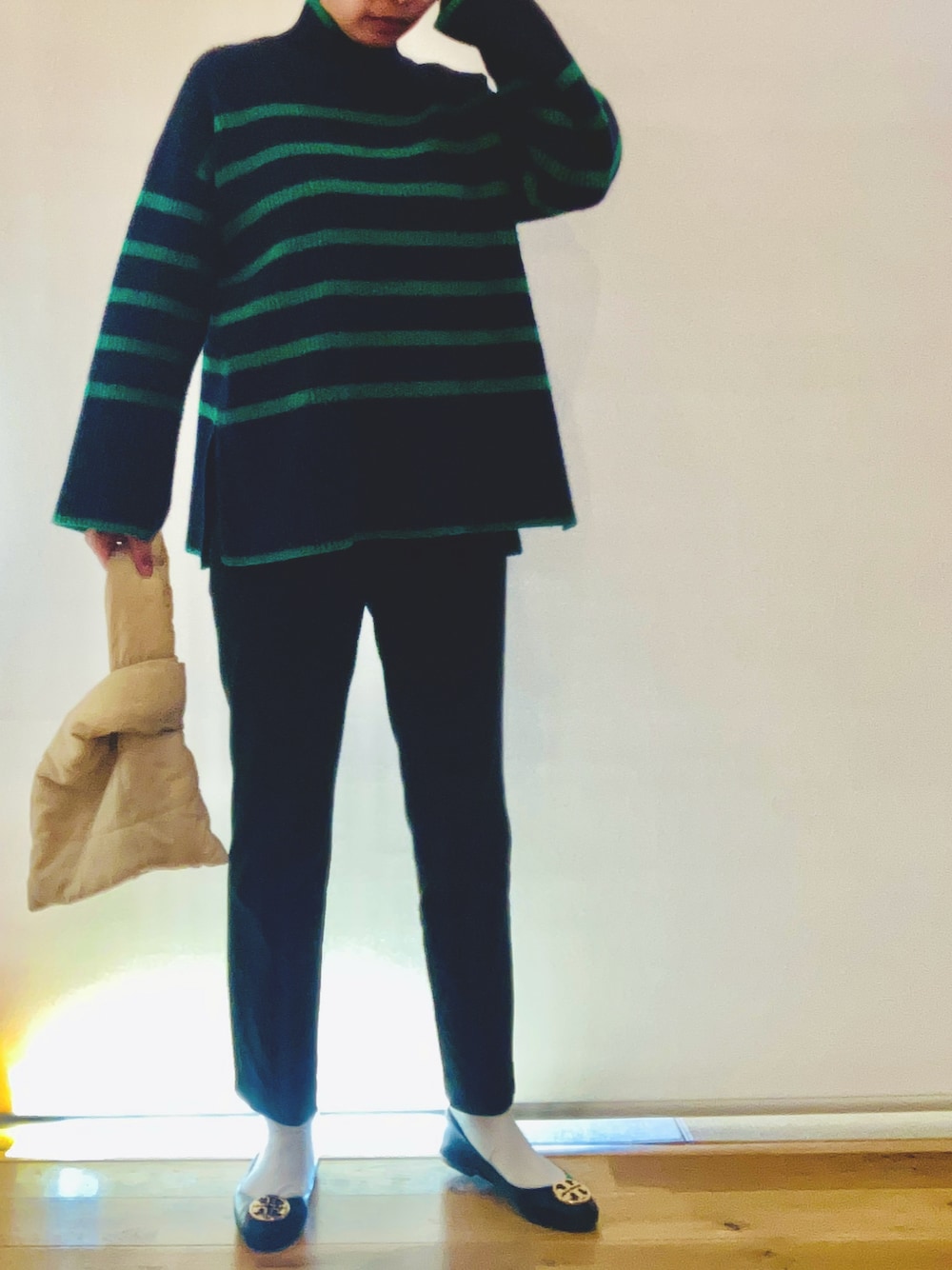 グリーン系のニット/セーター、ブラック系のスラックス、ベージュ系のハンドバッグを着用したレディースの冬コーディネートの1枚目の写真