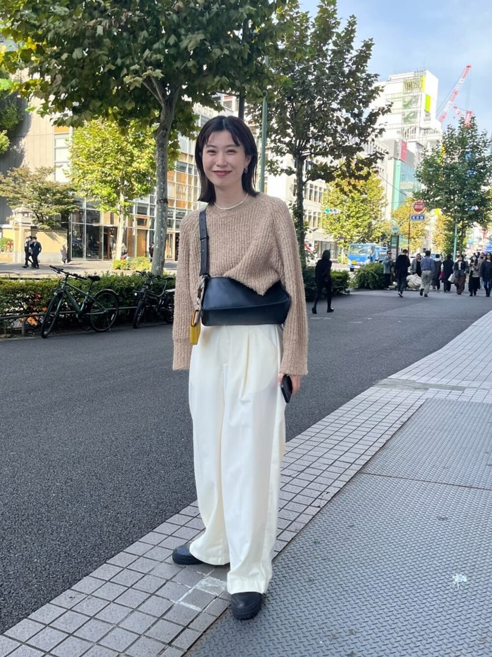 ブラック系のブーツ、ホワイト系のスラックス、ブラック系のショルダーバッグを着用したレディースの秋コーディネートの1枚目の写真