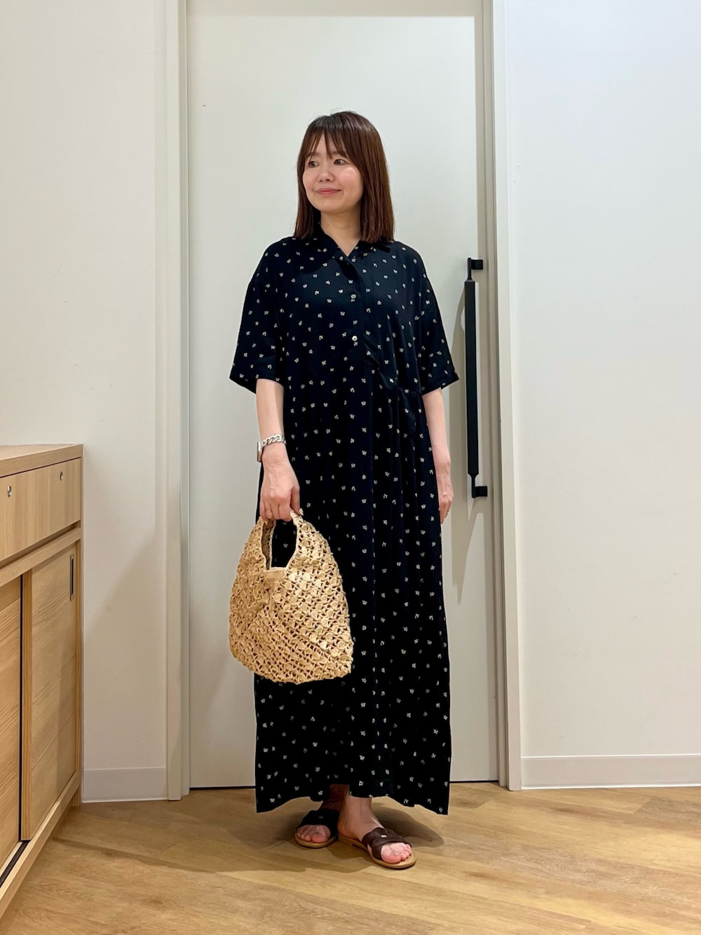 ブラック系のワンピース、ベージュ系のハンドバッグ、ブラウン系のサンダルを着用したレディースの夏コーディネートの1枚目の写真