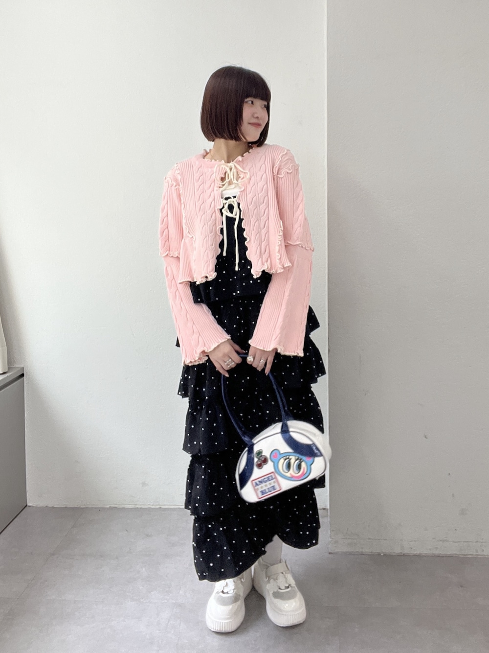 ブラック系のジャンパースカート、ピンク系のカーディガン/ボレロ、ブルー系のボストンバッグを着用したレディースの冬コーディネートの1枚目の写真