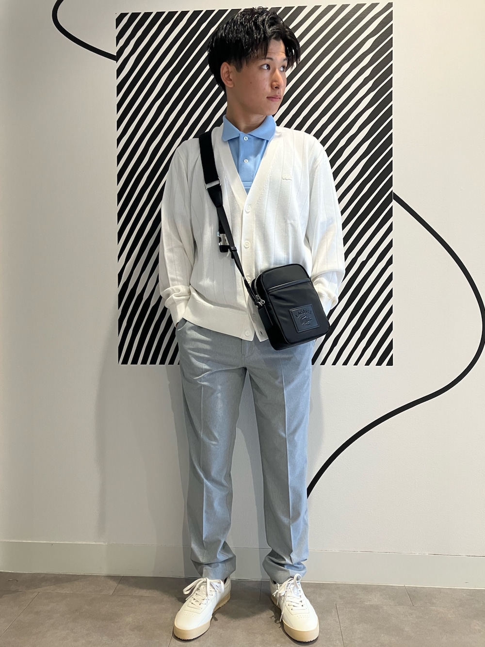 グレー系のチノパンツ、ブラック系のショルダーバッグ、ブルー系のポロシャツを着用したメンズの夏コーディネートの1枚目の写真