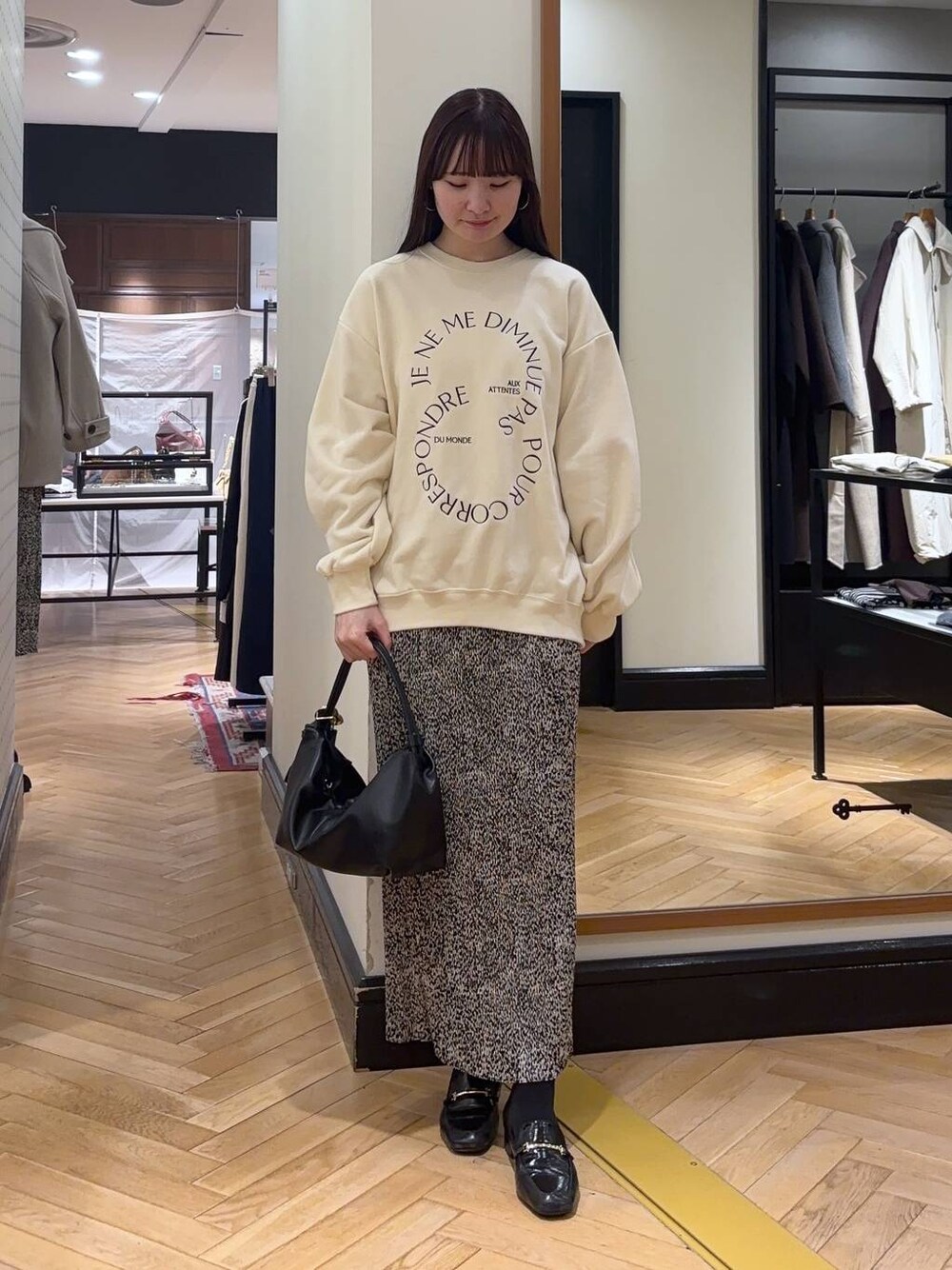 ブラック系のローファー、ベージュ系のスカート、ブラック系のショルダーバッグを着用したレディースの秋コーディネートの1枚目の写真