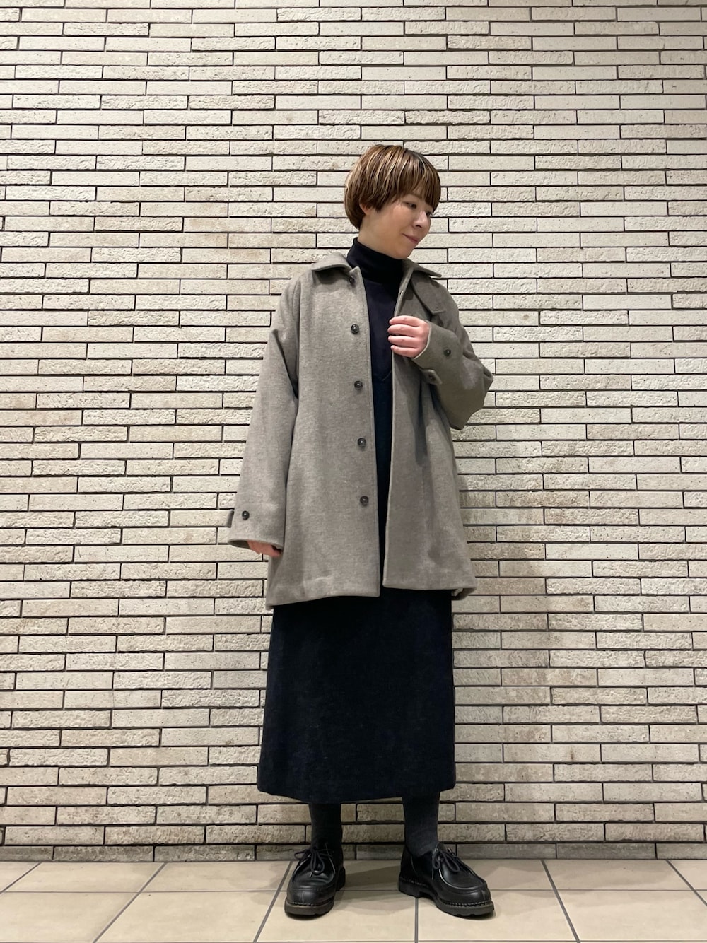 グレー系のステンカラーコート、グレー系のワンピースを着用したレディースの秋コーディネートの1枚目の写真