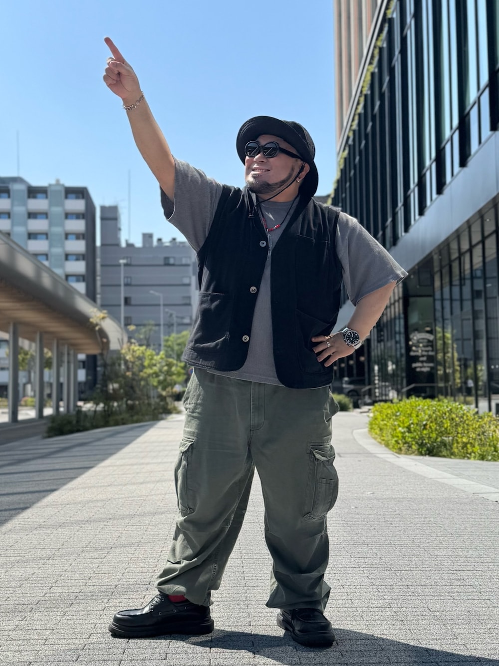 ブラック系のベスト、グレー系のTシャツ/カットソー、グリーン系のカーゴパンツを着用したメンズの春コーディネートの1枚目の写真