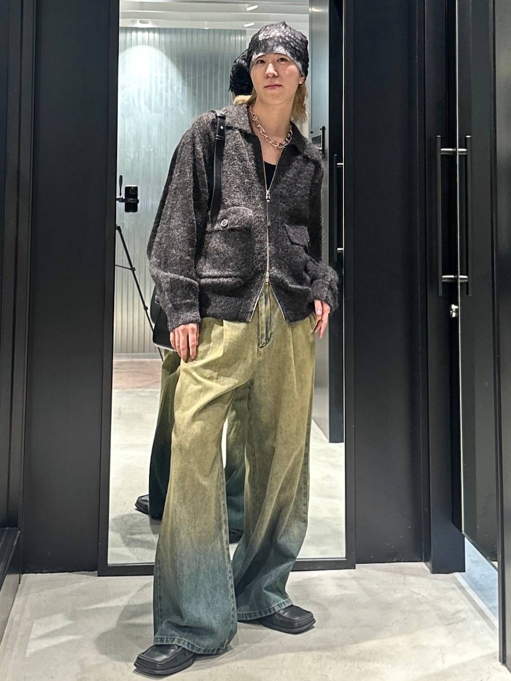 グリーン系のデニムパンツ、ブラック系のニット/セーター、ブラック系のショルダーバッグを着用したメンズの秋コーディネートの1枚目の写真