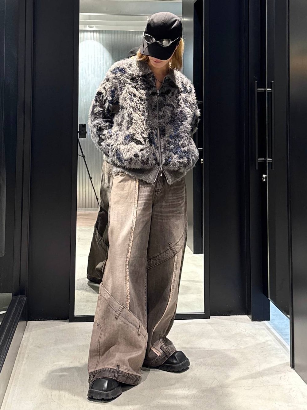 ブラウン系のデニムパンツ、グレー系のニット/セーター、ブラック系のキャップを着用したメンズの秋コーディネートの1枚目の写真