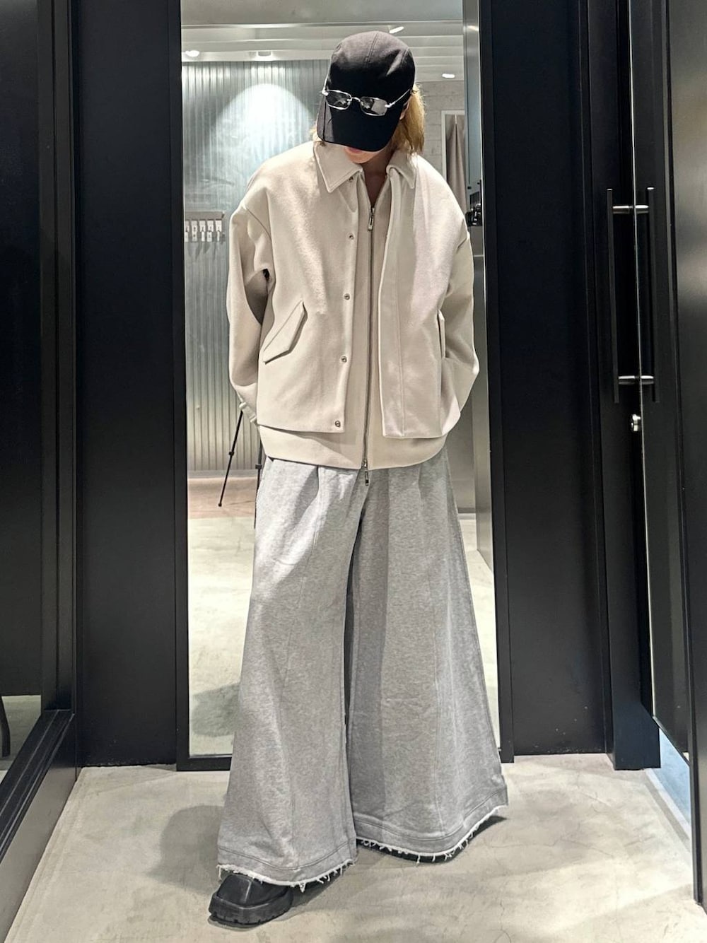 グレー系のスウェットパンツ、ホワイト系のブルゾン、ブラック系のキャップを着用したメンズの秋コーディネートの1枚目の写真