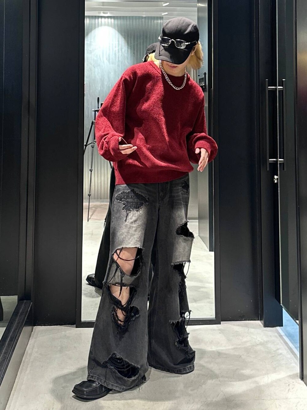 ブラック系のデニムパンツ、レッド系のニット/セーター、ブラック系のキャップを着用したメンズの秋コーディネートの1枚目の写真