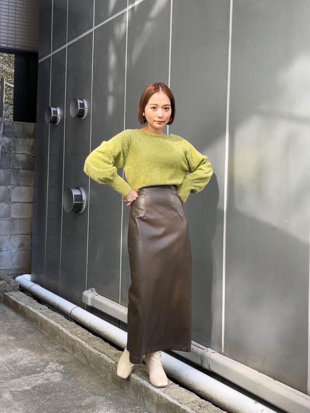 グリーン系のニット/セーター、ブラウン系のスカート、ホワイト系のブーツを着用したレディースの冬コーディネートの1枚目の写真