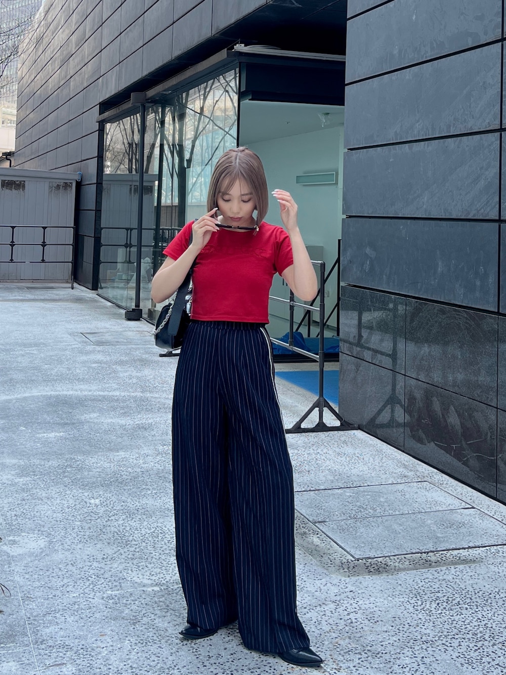 レッド系のTシャツ/カットソー、ブルー系のスラックス、ブラック系のショルダーバッグを着用したレディースの春コーディネートの1枚目の写真