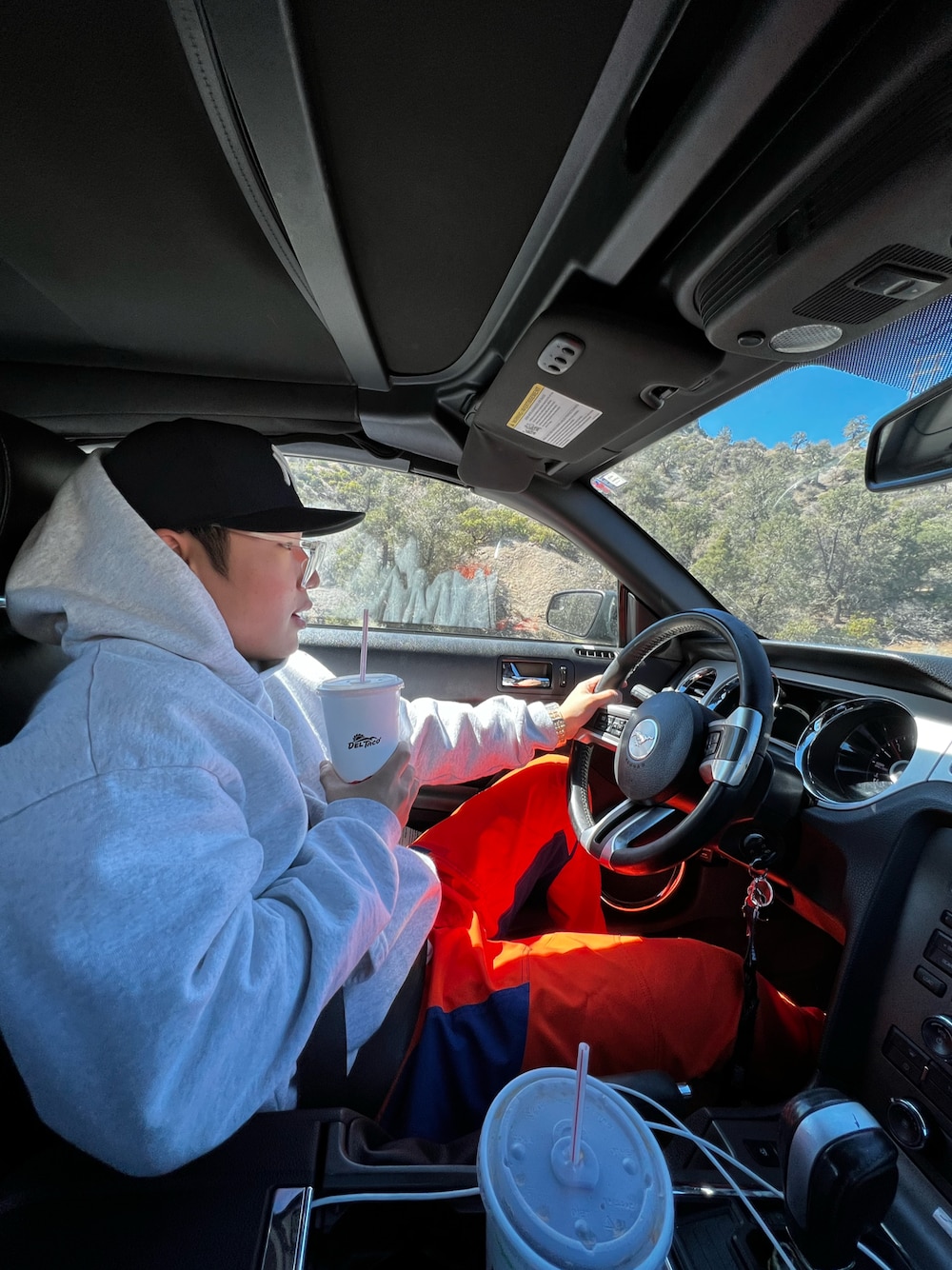 グレー系のパーカー、オレンジ系のパンツ、ブラック系のキャップを着用したメンズの夏コーディネートの1枚目の写真