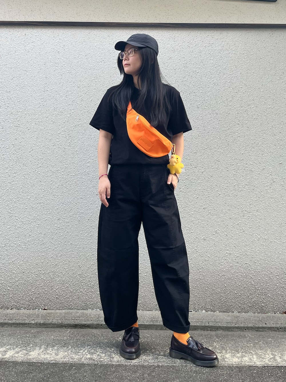 オレンジ系のショルダーバッグ、ブラック系のTシャツ/カットソー、ブラック系のパンツを着用したレディースの秋コーディネートの1枚目の写真