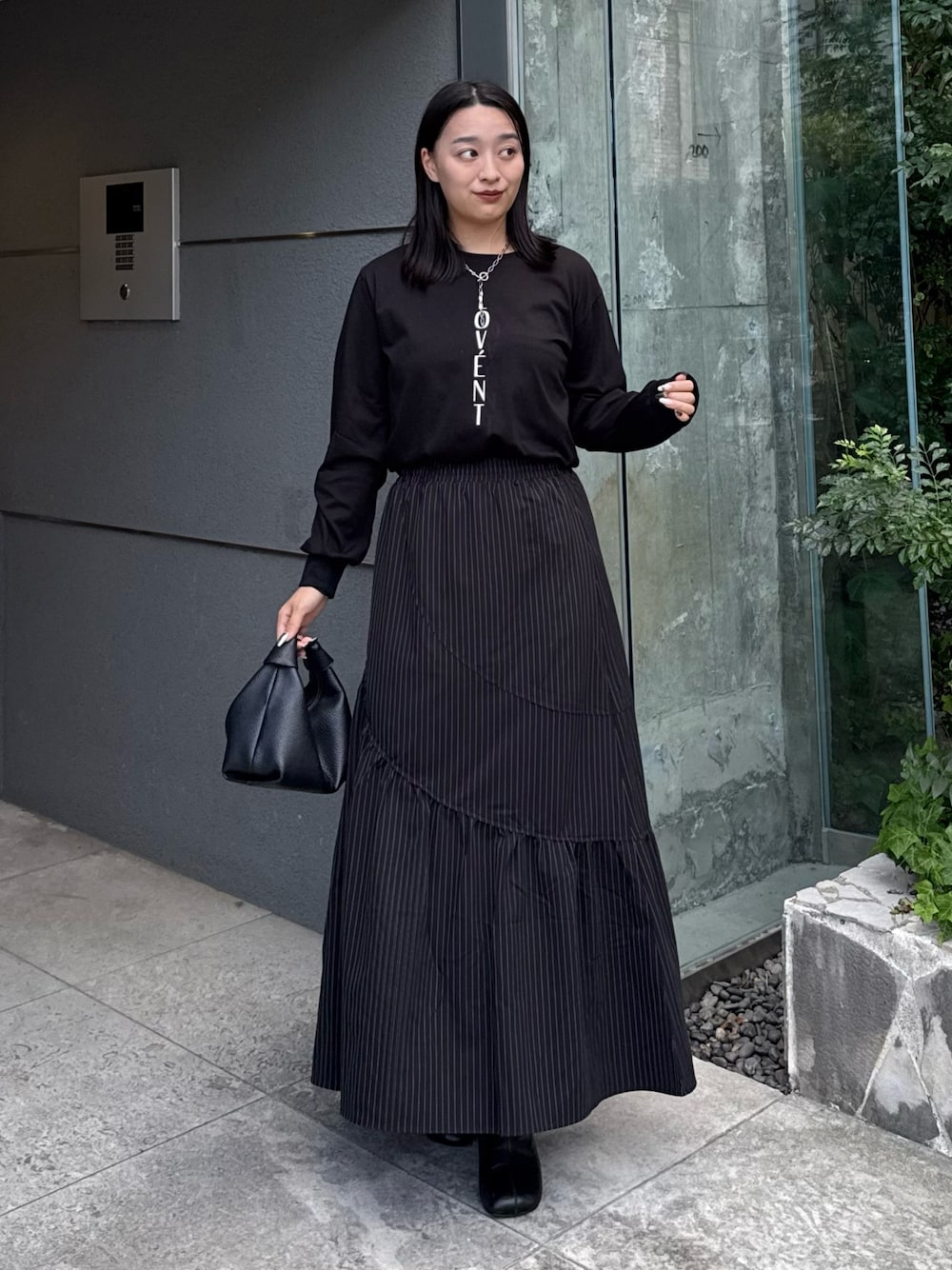 ブラック系のTシャツ/カットソー、ブラック系のスカート、ブラック系のトートバッグを着用したレディースの秋コーディネートの1枚目の写真