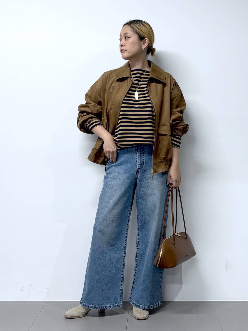 ブルー系のデニムパンツ、ブラウン系のトートバッグ、ベージュ系のTシャツ/カットソーを着用したレディースの秋コーディネートの1枚目の写真