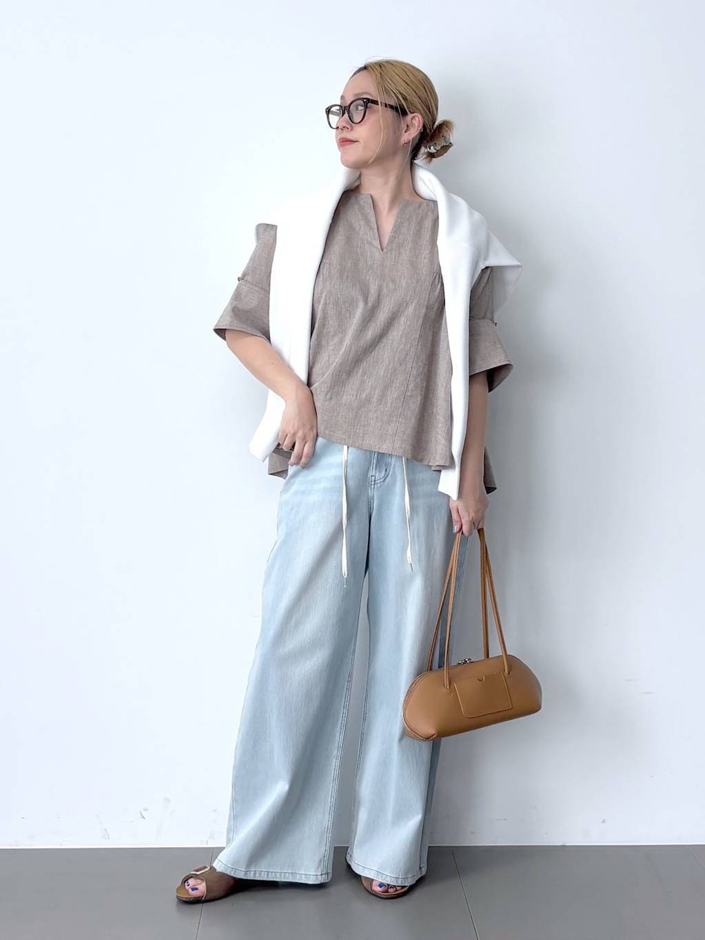 ブルー系のデニムパンツ、ベージュ系のシャツ/ブラウス、ブラウン系のハンドバッグを着用したレディースの春コーディネートの1枚目の写真