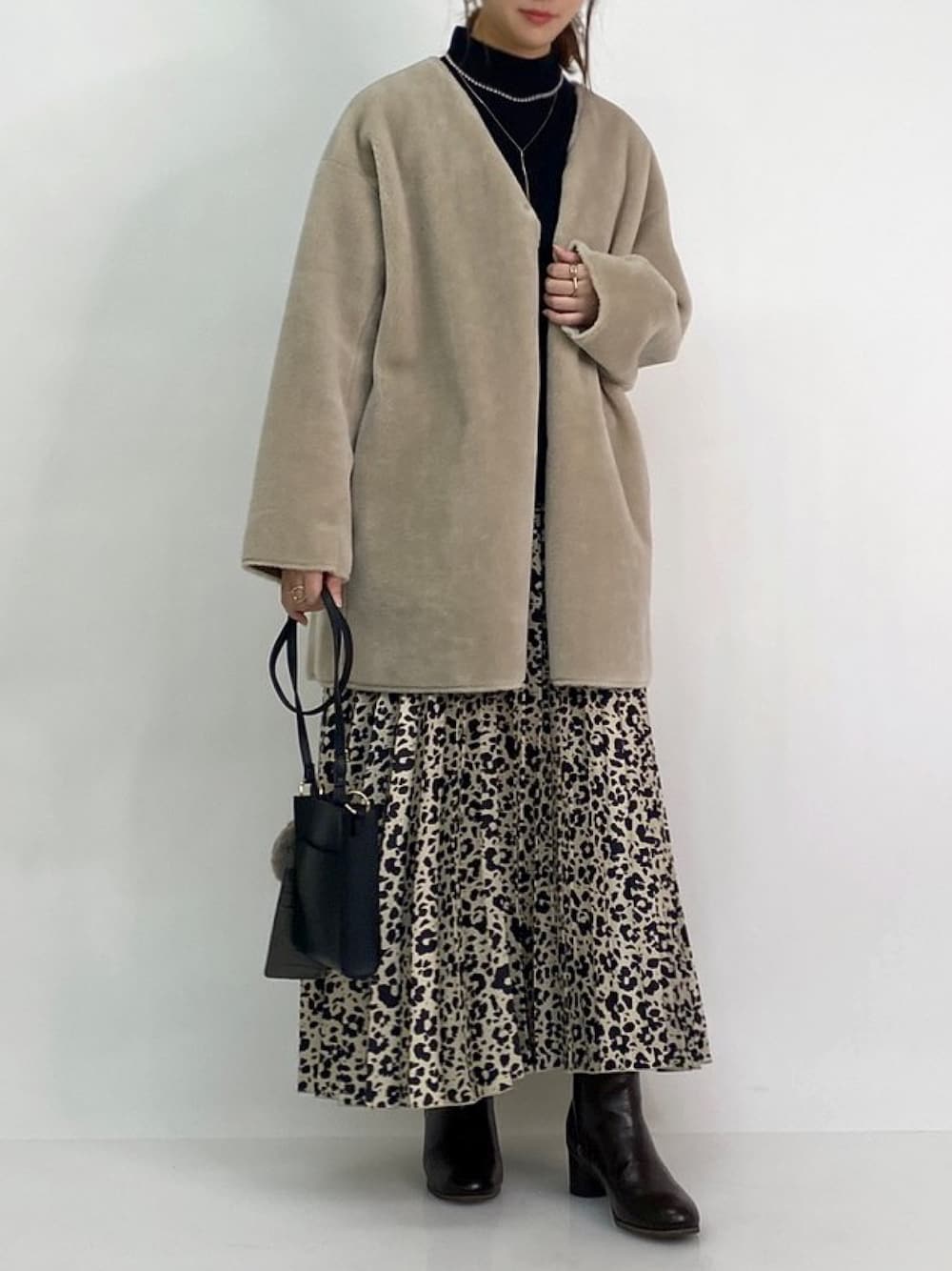 ベージュ系のノーカラーコート、ブラック系のブーツ、ベージュ系のスカートを着用したレディースの冬コーディネートの1枚目の写真