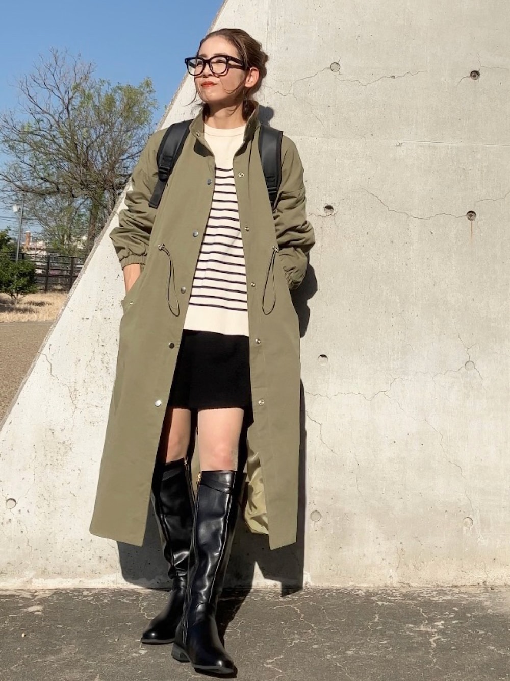 グリーン系のステンカラーコート、ブラック系のバックパック/リュック、ブラウン系のブーツを着用したレディースの秋コーディネートの1枚目の写真