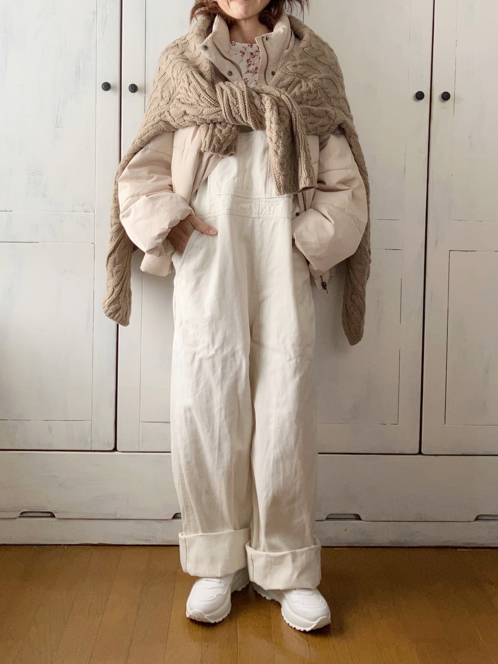 ホワイト系のダウンジャケット/コート、ベージュ系のカーディガン/ボレロ、ホワイト系のサロペット/オーバーオールを着用したレディースの冬コーディネートの1枚目の写真