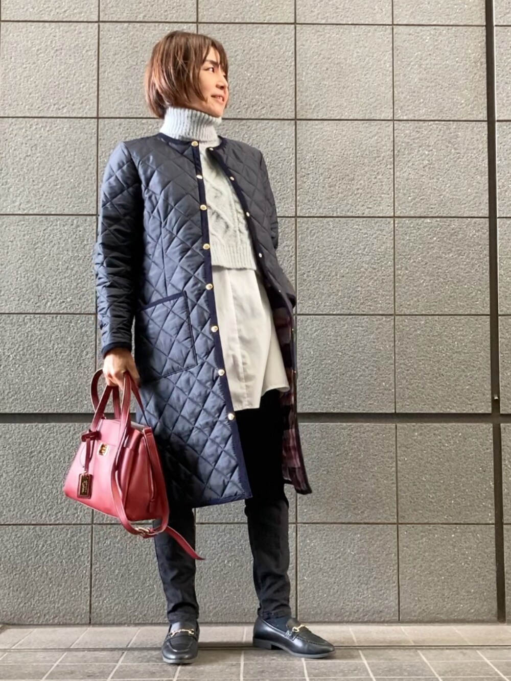 ブルー系のノーカラーコート、グレー系のニット/セーター、ブラック系のデニムパンツを着用したレディースの秋コーディネートの1枚目の写真