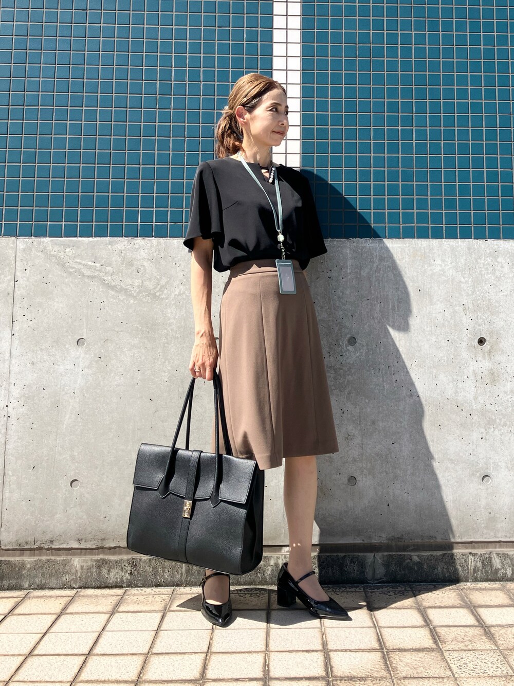 ブラック系のシャツ/ブラウス、ブラウン系のスカート、ブラック系のビジネスバッグを着用したレディースの夏コーディネートの1枚目の写真