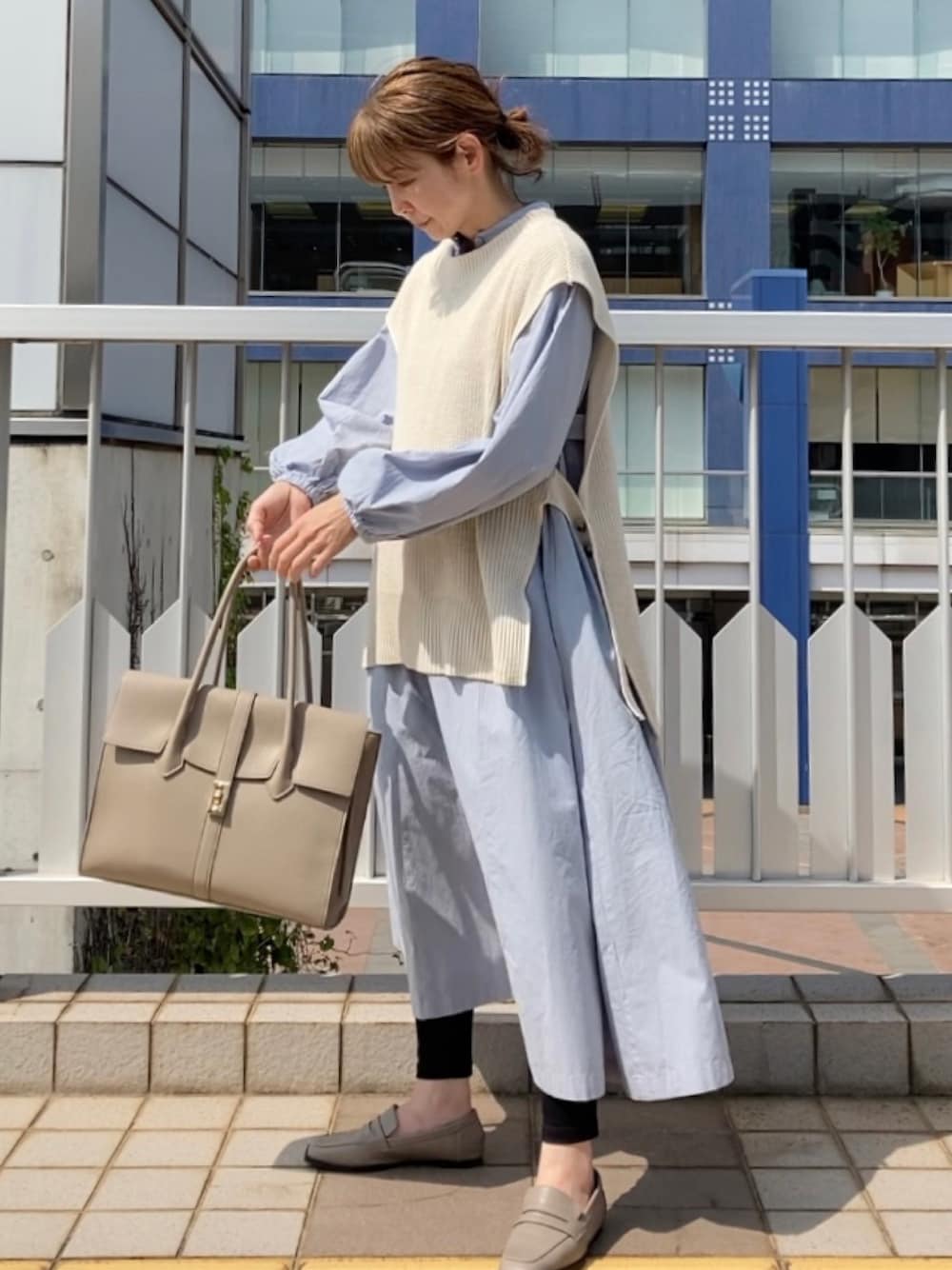 ホワイト系のベスト、ブルー系のシャツワンピース、ベージュ系のビジネスバッグを着用したレディースの春コーディネートの1枚目の写真