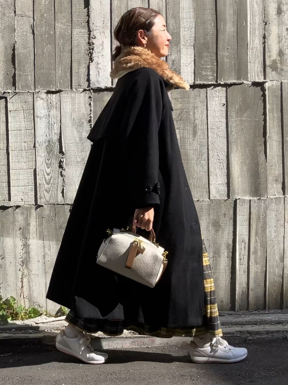 ベージュ系のボストンバッグ、ホワイト系のスニーカー、イエロー系のスカートを着用したレディースの冬コーディネートの1枚目の写真