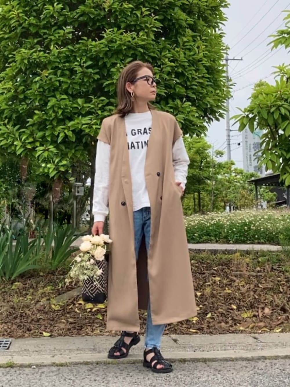 ベージュ系のワンピース、ブルー系のデニムパンツ、ブラック系のかごバッグを着用したレディースの春コーディネートの1枚目の写真