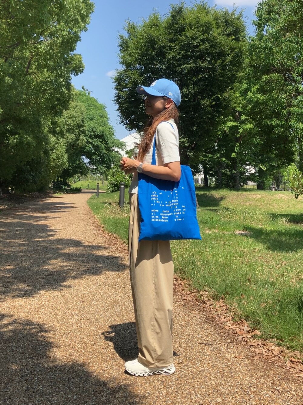 ベージュ系のパンツ、ホワイト系のポロシャツ、ブルー系のトートバッグを着用したレディースの夏コーディネートの1枚目の写真