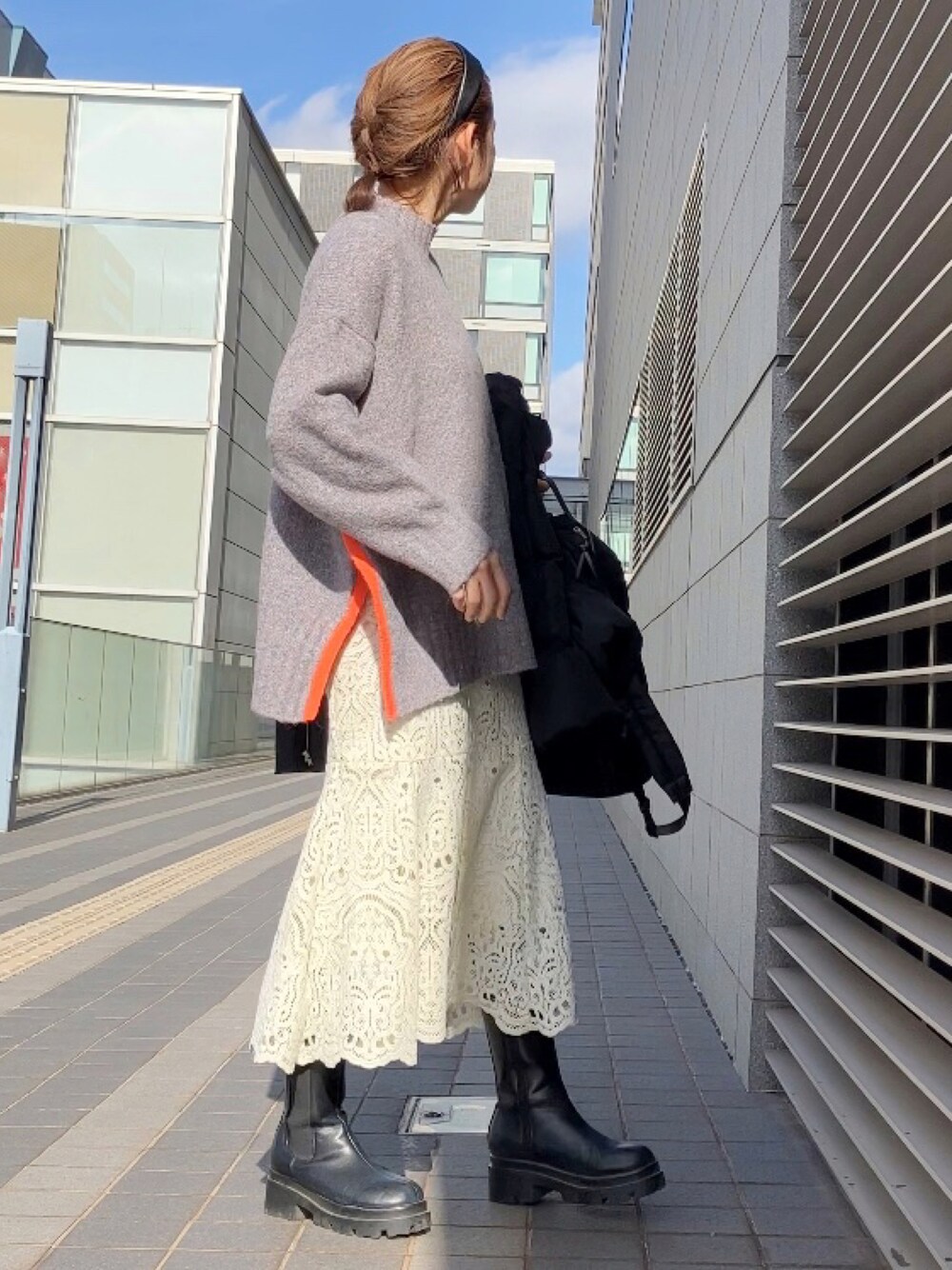 グレー系のニット/セーター、ホワイト系のスカート、ブラック系のブーツを着用したレディースの冬コーディネートの1枚目の写真