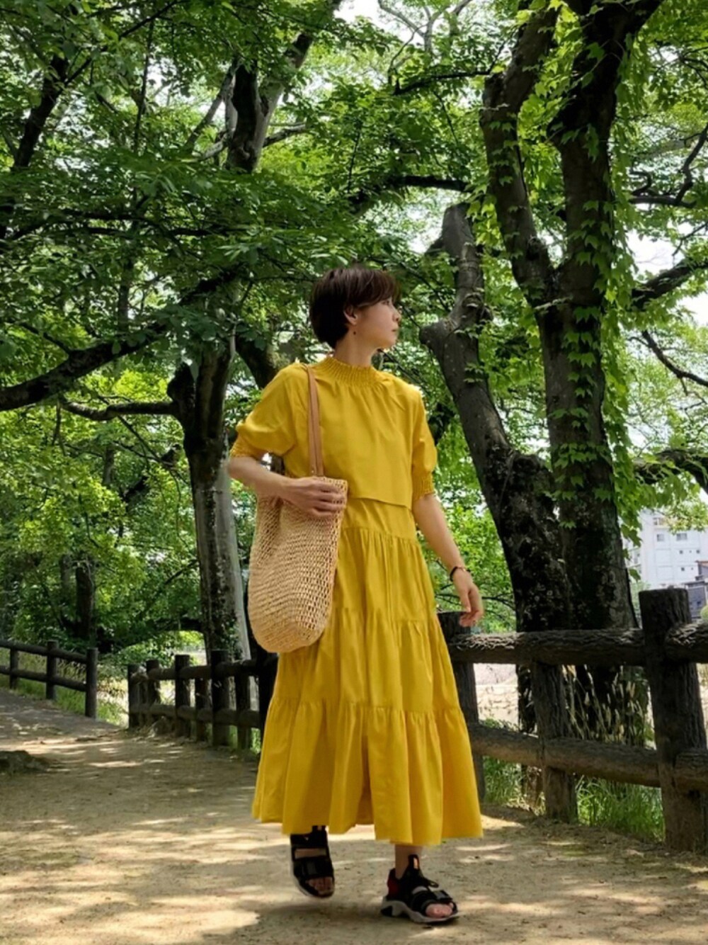 イエロー系のワンピース、ベージュ系のバッグ、グレー系のサンダルを着用したレディースの夏コーディネートの1枚目の写真