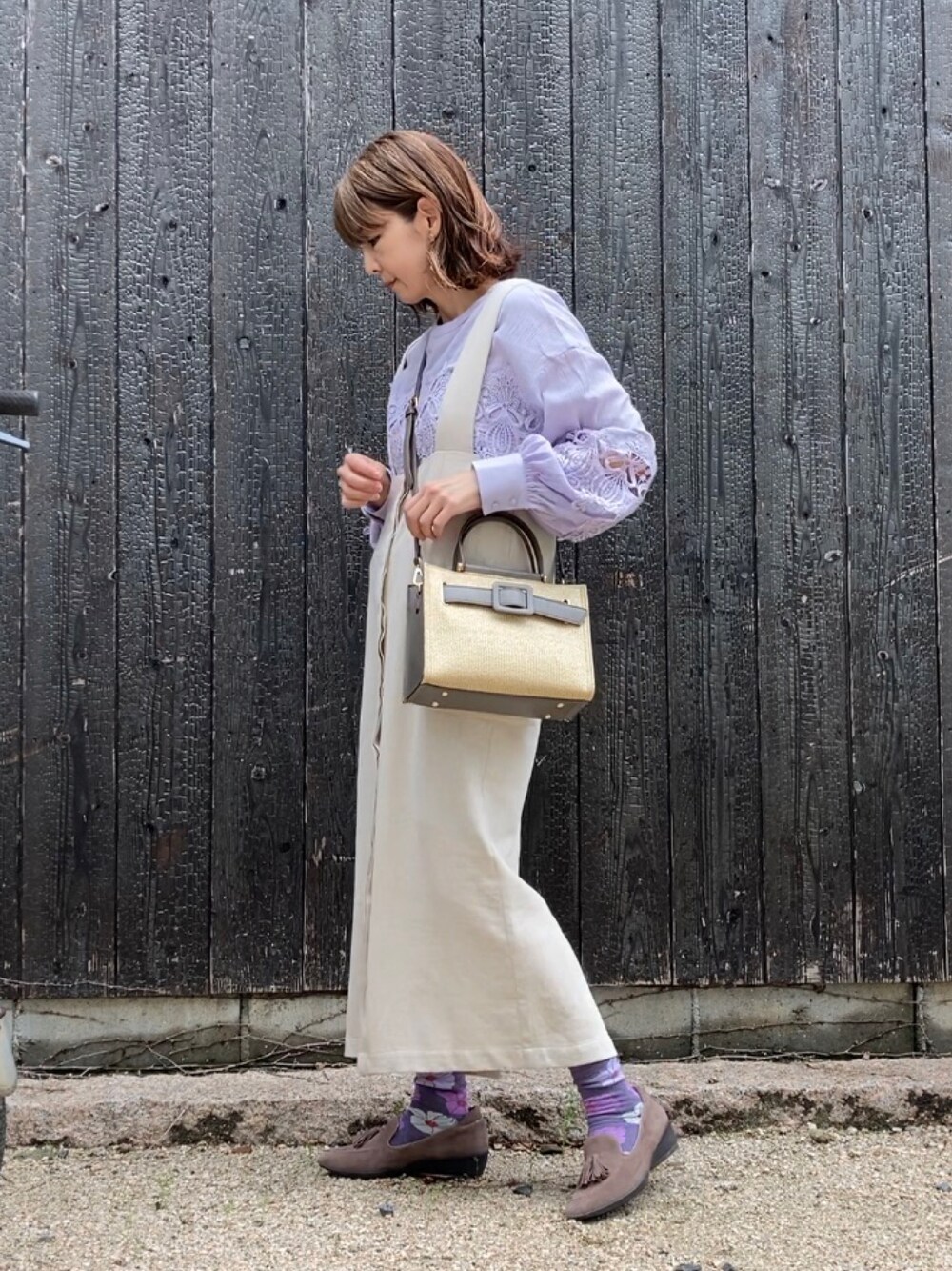 グレー系のハンドバッグ、パープル系のシャツ/ブラウス、ベージュ系のジャンパースカートを着用したレディースの春コーディネートの1枚目の写真