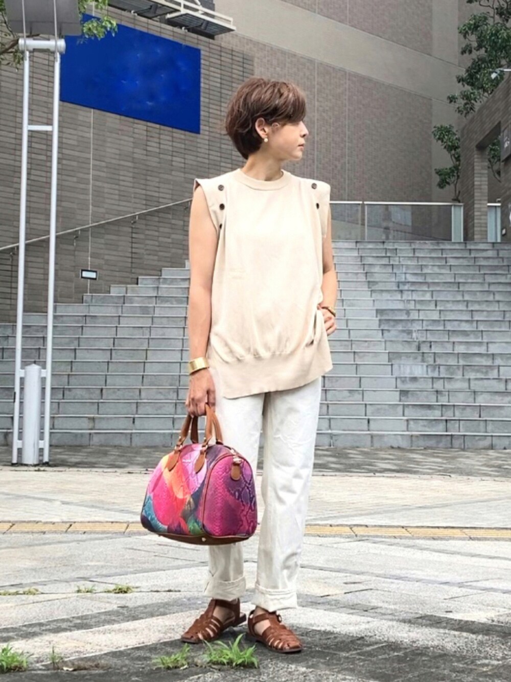 レッド系のハンドバッグ、ベージュ系のニット/セーター、ホワイト系のデニムパンツを着用したレディースの夏コーディネートの1枚目の写真