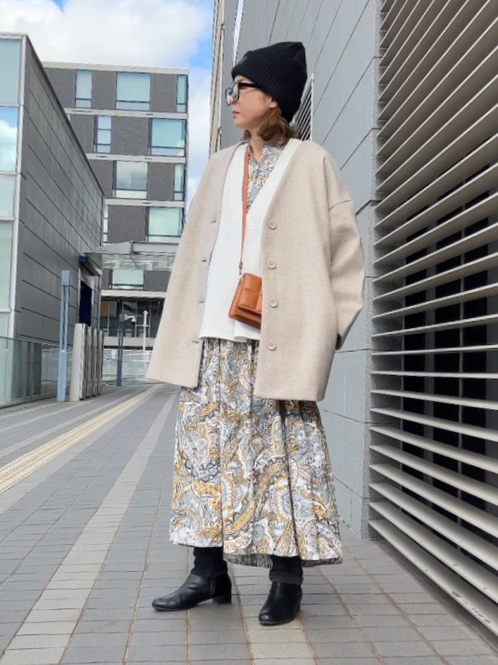 イエロー系のワンピース、ブラウン系のクラッチバッグ、ブラック系のブーツを着用したレディースの冬コーディネートの1枚目の写真