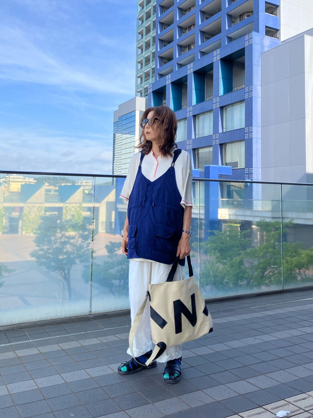ブルー系のベスト、ベージュ系のトートバッグ、ホワイト系のTシャツ/カットソーを着用したレディースの夏コーディネートの1枚目の写真